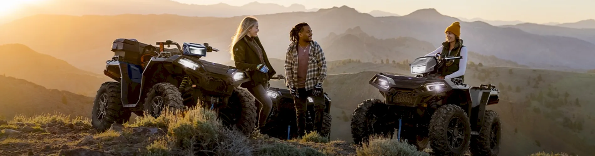 Three people with ATVs parked on a mountain trail at sunset
