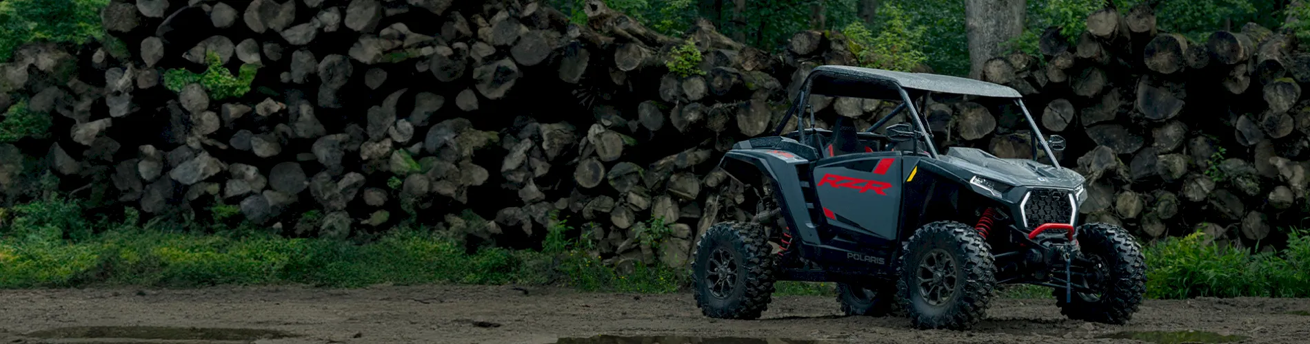 Polaris RZR side-by-side parked in front of a large stack of logs