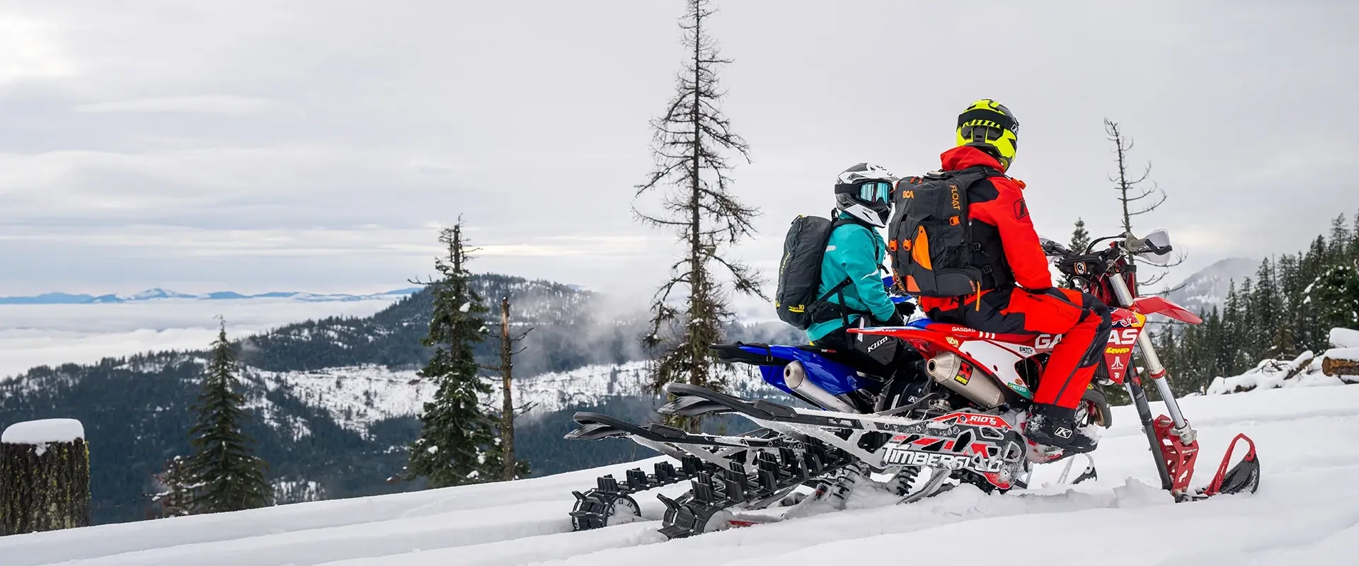 Two people riding a Polaris Timbersled in a snowy mountain landscape